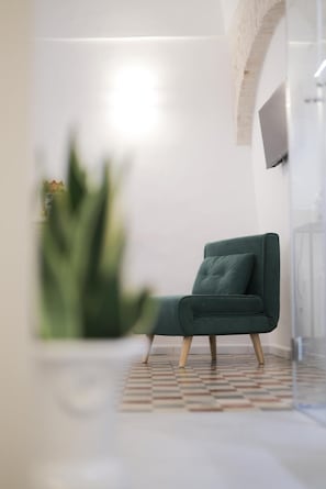 A modern room with a green chair, a patterned floor, and a TV mounted on the wall. - Room 'Pepenero Apulian Rooms - Loggetta' with Wi-Fi and Air Conditioning (Noci)
