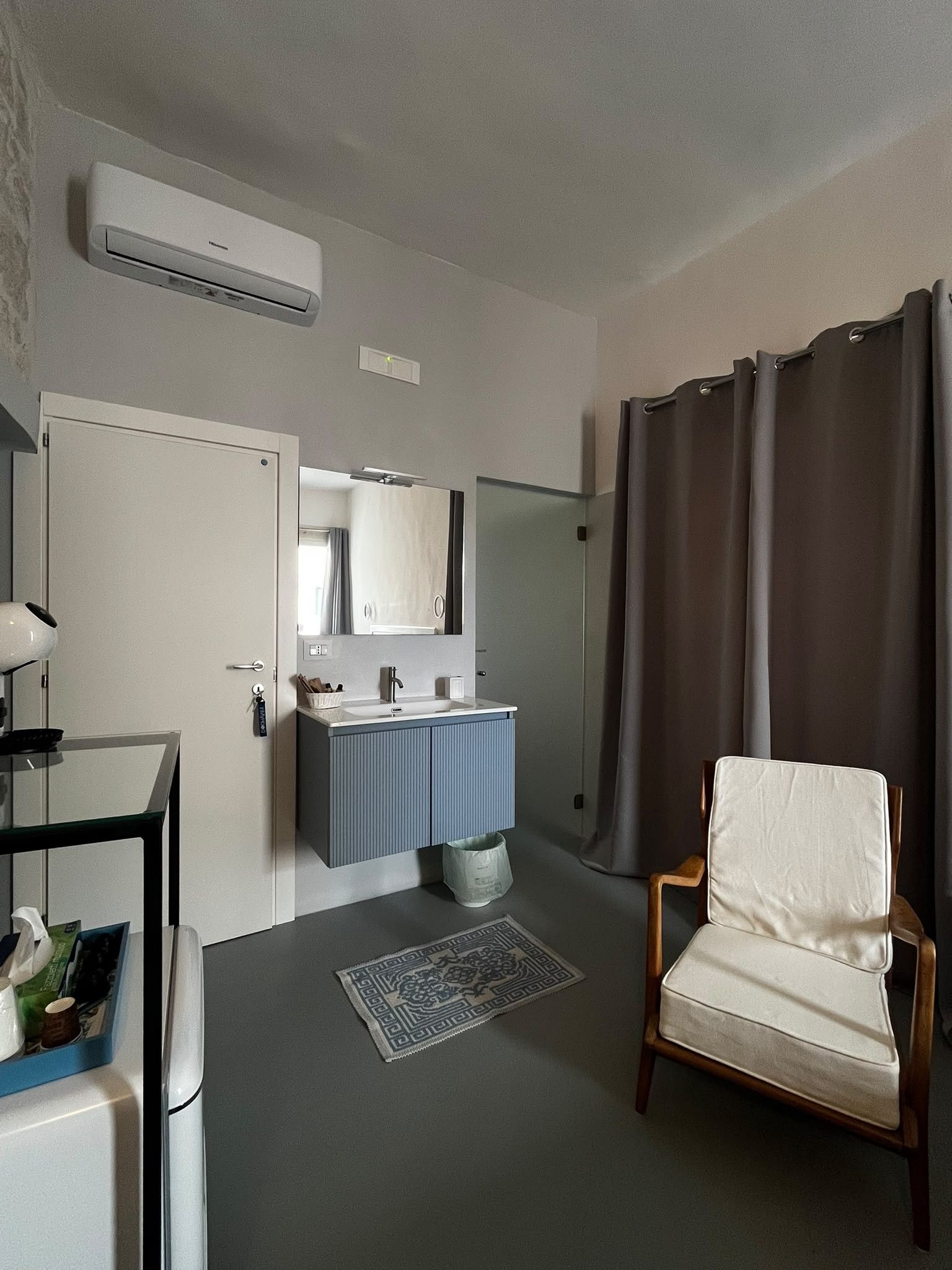 A hotel room with a bathroom, a chair, a sink, and a mirror.