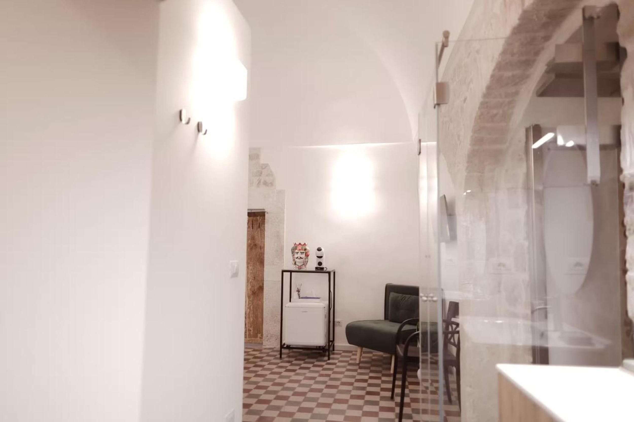 A hallway with a checkered floor, a chair, and a small table with decorative items.