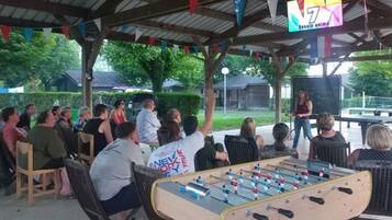 An outdoor gathering with people seated and standing, a foosball table, and a banner with '7' and 'Dessin anime' visible.