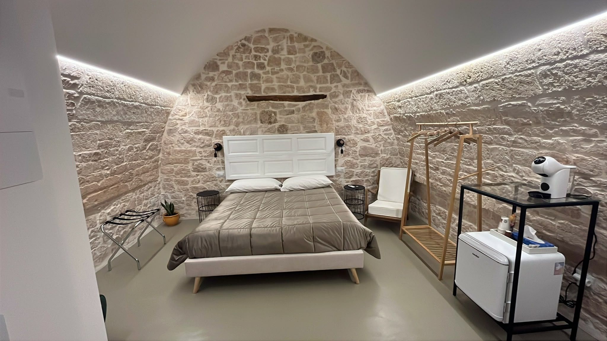 A bedroom with a stone wall, a bed, a chair, a drying rack, and a hairdryer.