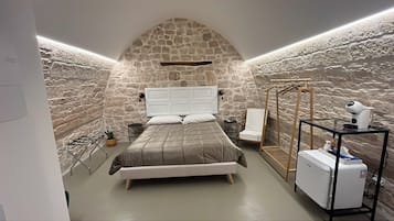 A bedroom with a stone wall, a bed, a chair, a drying rack, and a hairdryer.