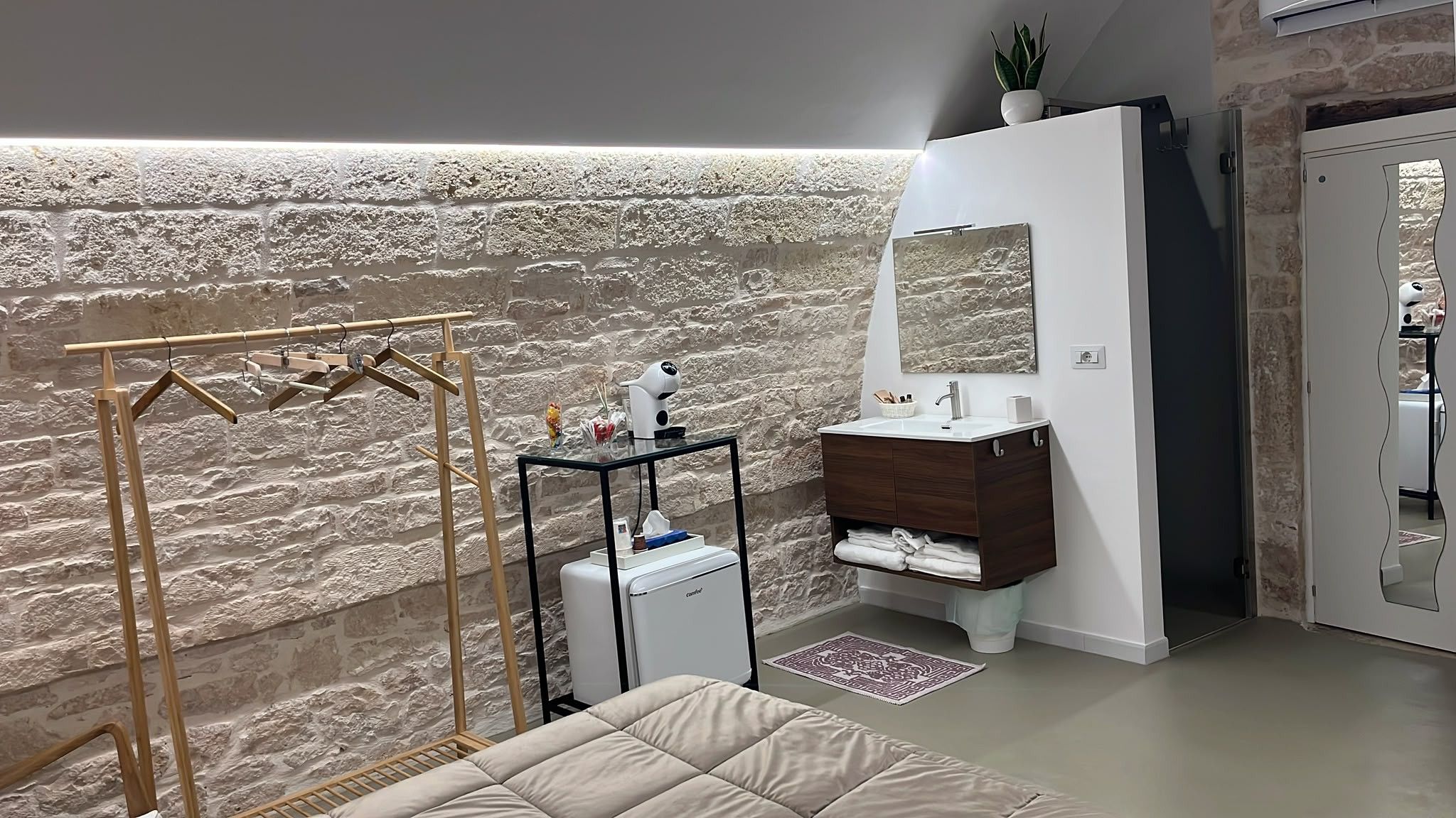 A bathroom with a stone wall, a wooden drying rack, a white sink, and a mirror.