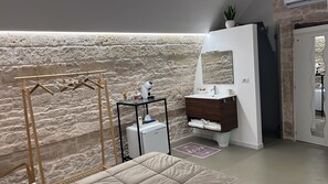 A bathroom with a stone wall, a wooden drying rack, a white sink, and a mirror. - Room 'Pepenero Apulian -Pietra Viva' with Wi-Fi and Air Conditioning (Noci)