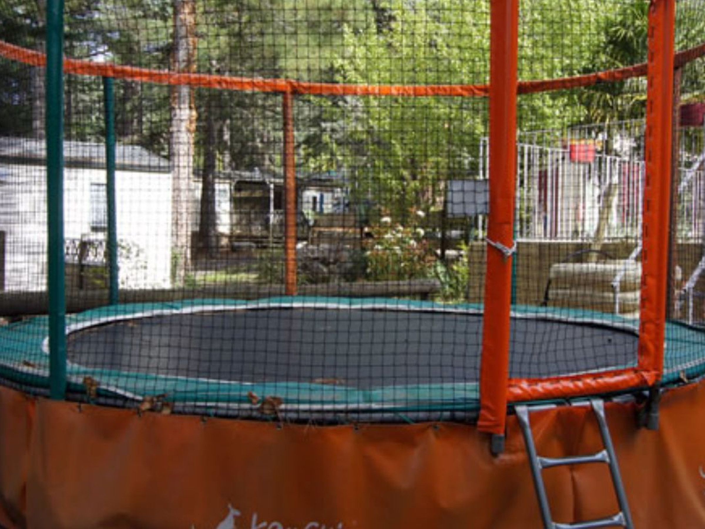 Een trampoline met veiligheidsnet, omringd door een hek.