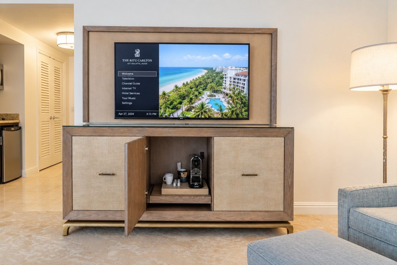 A hotel room with a flat-screen TV mounted on a wooden cabinet, a coffee maker, and a remote control on the cabinet's surface.