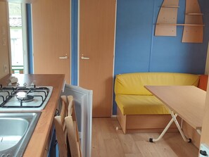 Une cuisine de taille réduite, équipée d’une cuisinière à gaz, d’un évier et d’un banc jaune.