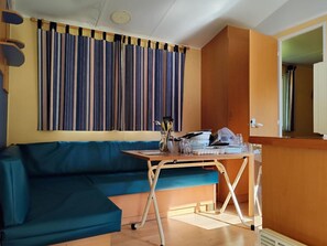 Une pièce avec un canapé bleu, une table en bois sur laquelle se trouve de l’ustensile de cuisine, et un rideau à rayures.