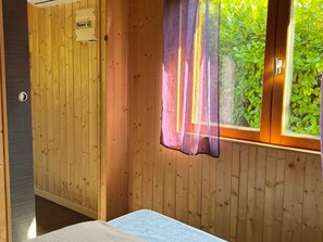 A wooden room with a bed, a window with a curtain, and a door with a lock. - Cozy chalet with AC - 2 guests, pets welcome (Angicourt)