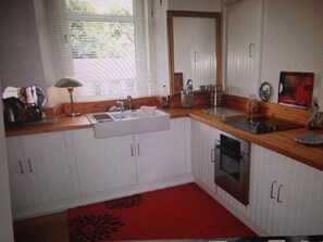 A kitchen with white cabinets, a red rug, a window, and a sink. - Stunning sea views and scenic walks (Kirn)