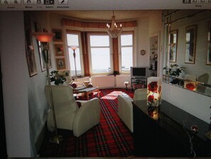 A living room with a red plaid carpet, a chandelier, a television, and a mirror. - Stunning sea views and scenic walks (Kirn)