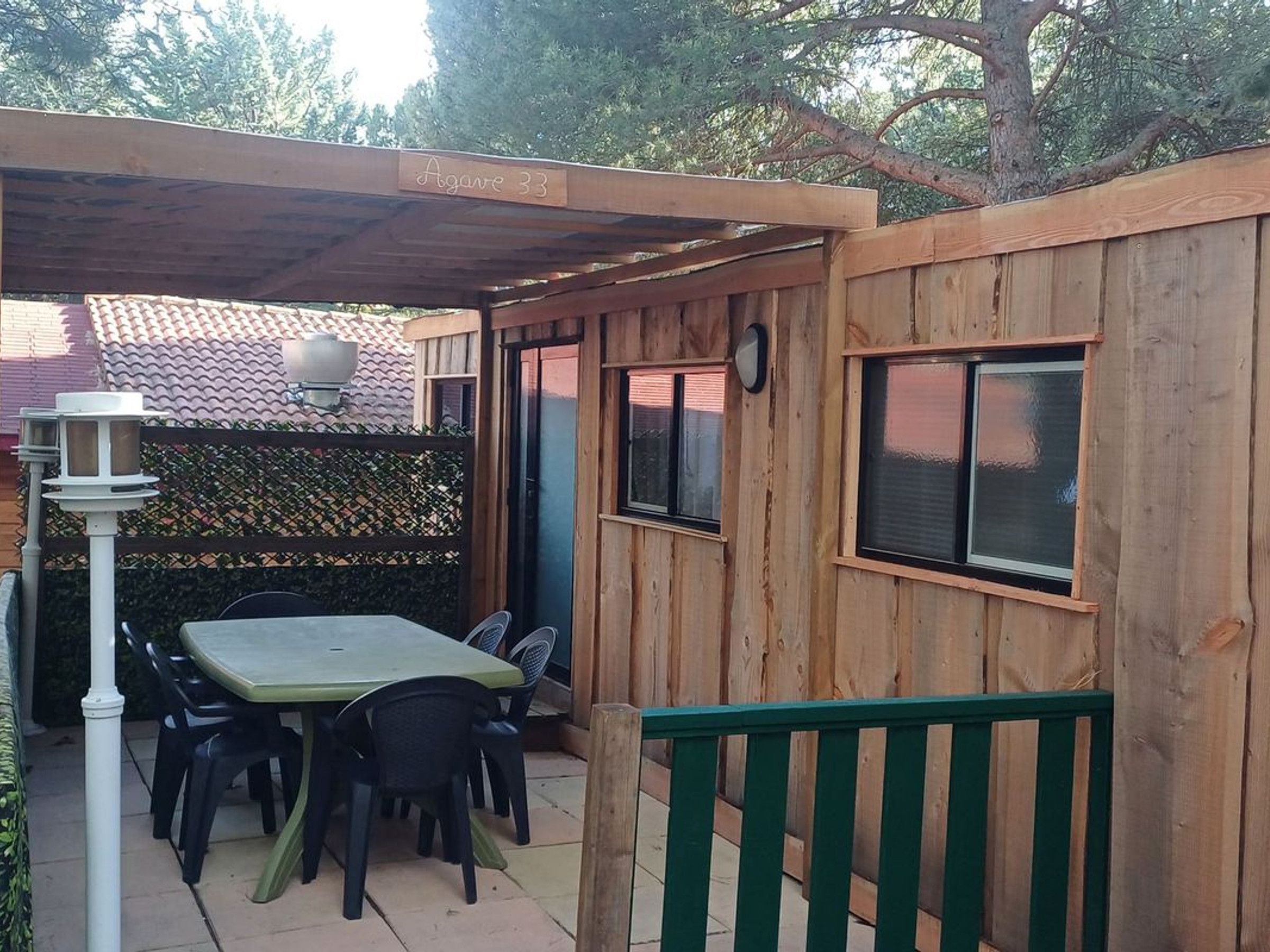 A covered patio area with a table and chairs, a wooden fence, and a green gate.