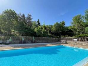 A clear blue swimming pool with a wooden deck, surrounded by a stone wall and a wooden fence.