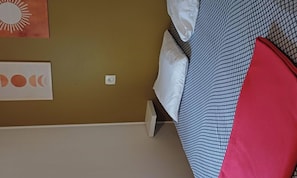 Una cama con una colcha estampada, un almohárraga roja y una pared con un adorno de sol y luna.