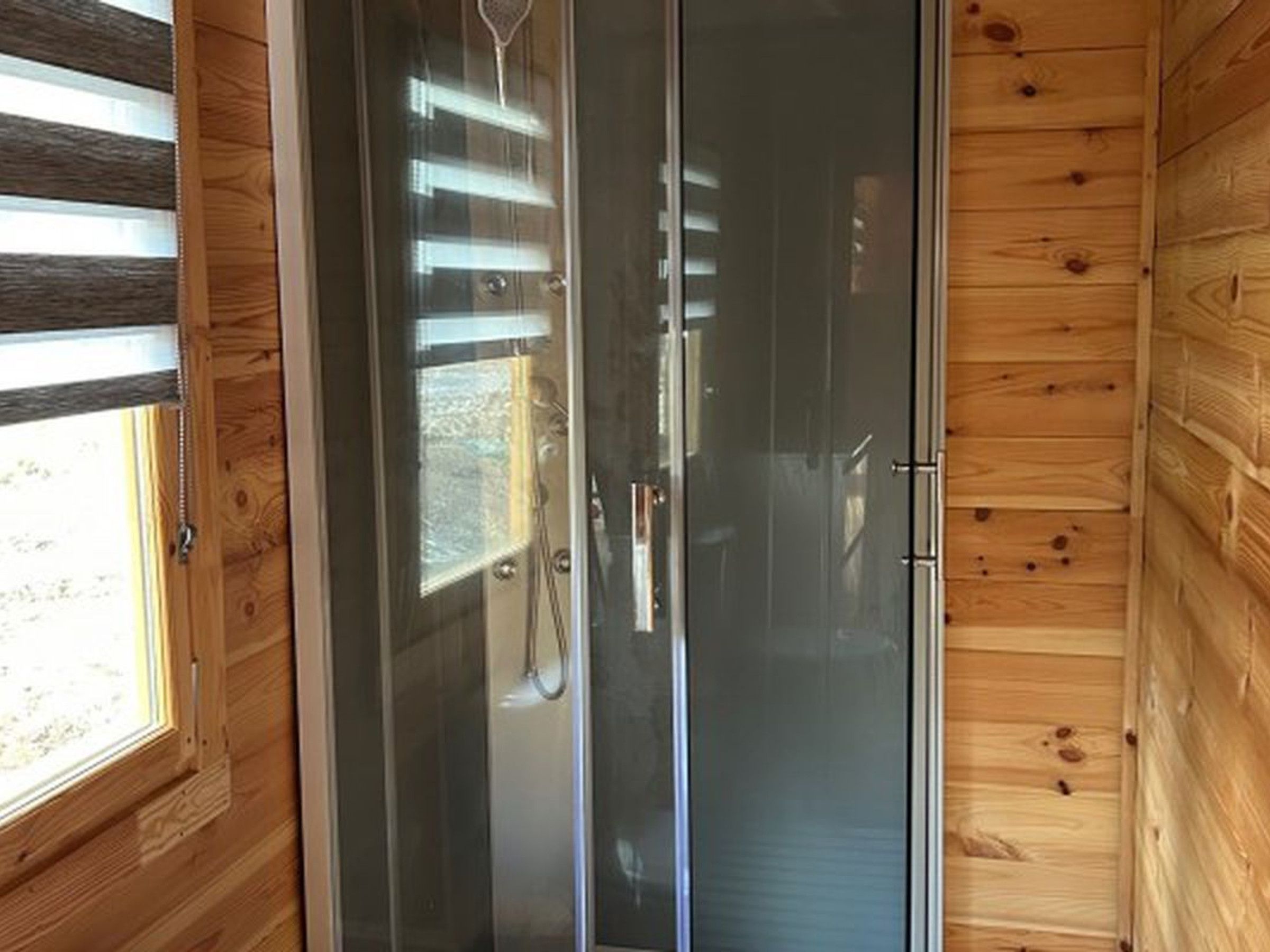 Une cabane en bois dotée d’une porte coulissante en verre donnant accès à un espace douche.