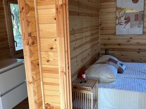 A wooden cabin room with a bed, pillows, a nightstand, and a window. - Chalet with AC - 4 guests (Linguizzetta)
