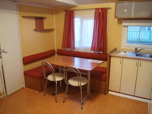 A compact kitchenette with a window, a sink, and a dining area with a bench and chairs. - Mobile home with AC, pets OK - 6 guests (Sournia)