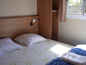 A bed with white pillows and a bamboo-patterned bedspread, a wooden headboard, a power outlet, and a window with curtains. - Chalet pets welcome - 7 guests (Pleaux)