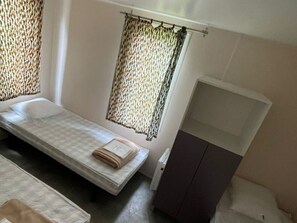 Ein kleines Zimmer mit einem Einzelbett, einem Kleiderschrank und einem Fenster mit gemusterten Vorhängen.
