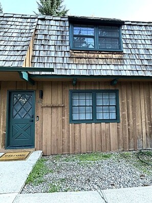 A wooden building with a shingled roof, a green door, and two windows.