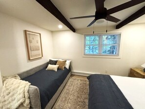 A bedroom with two beds, a ceiling fan, a window with blinds, and a framed picture on the wall.