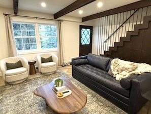 A living room with a dark sofa, two armchairs, a wooden coffee table, and a staircase with a railing.