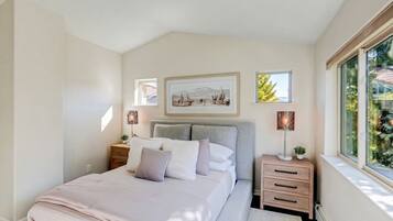 Ein Schlafzimmer mit einem Bett, Nachttischen, einem Fenster und Wandbildern.