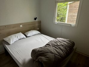 Una cama individual con cabecera de madera, ropa de cama blanca y ventana con vistas al exterior.