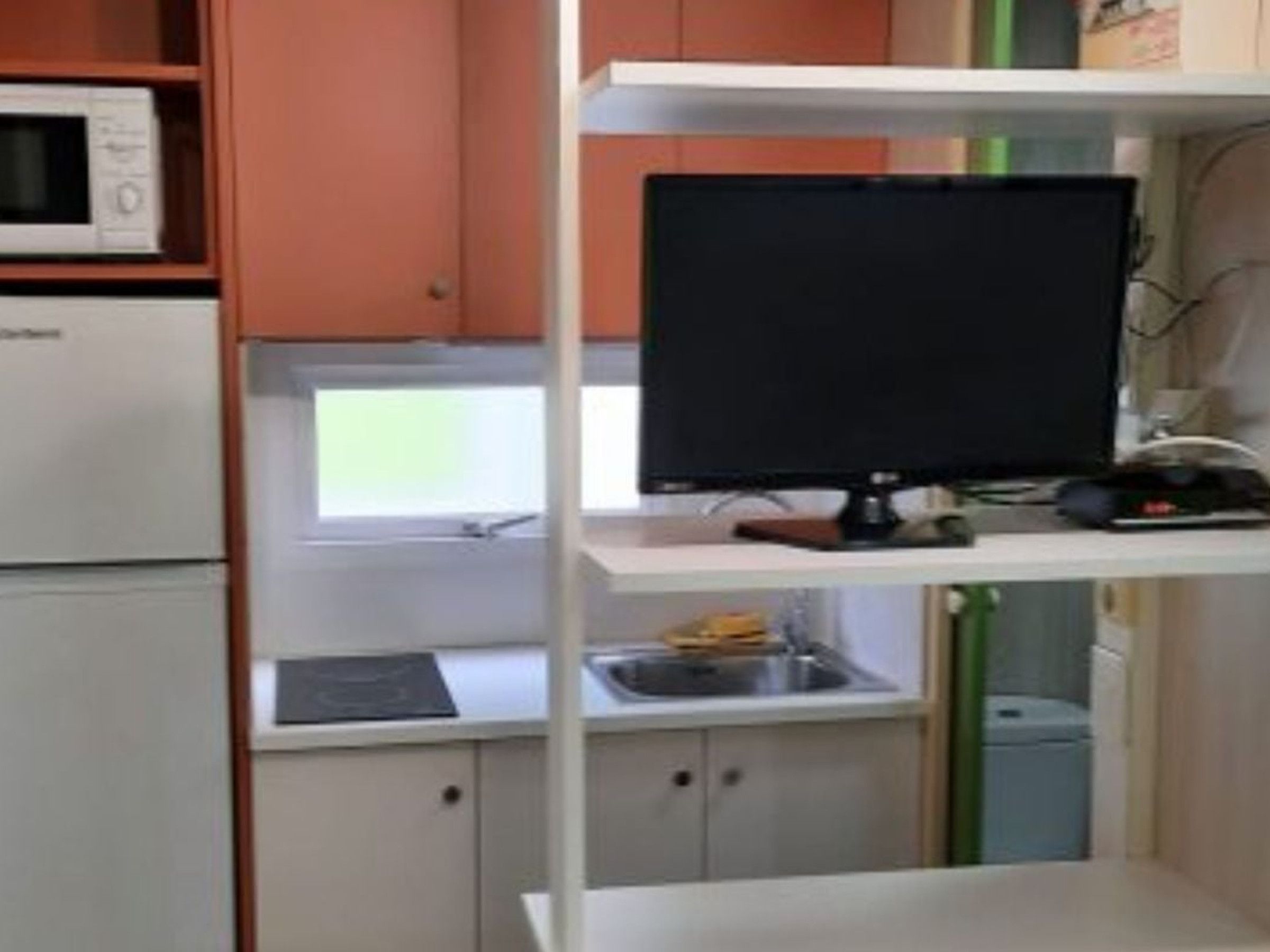 Una kitchenette con microondas, un monitor de computadora sobre una repisa y un lavamanos.