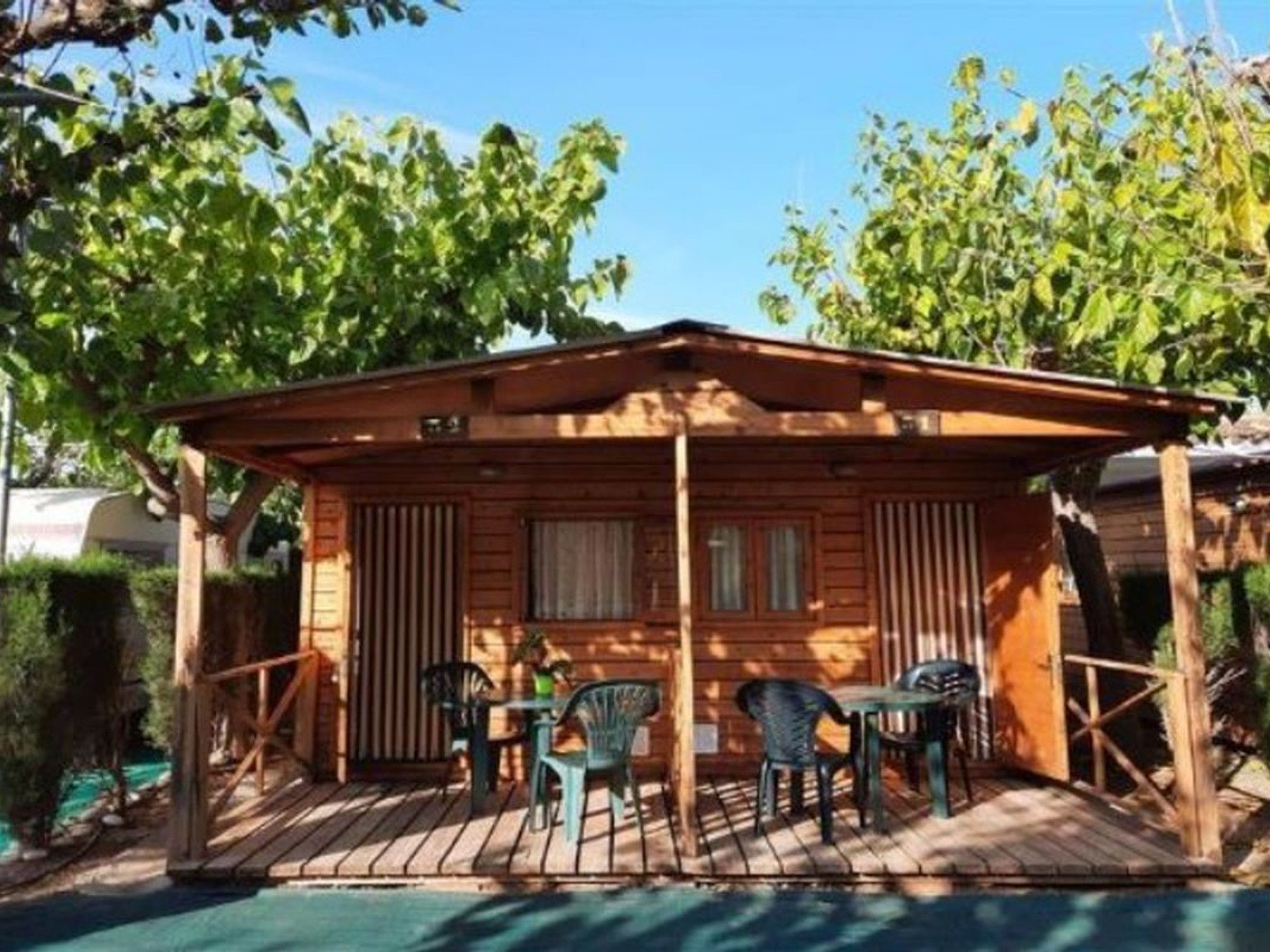 Una cabaña de madera con un porche cubierto, dos mesas y cuatro sillas.