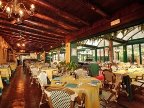 A restaurant with wooden beams and chandeliers, tables set with yellow tablecloths and wicker chairs, and a view of greenery outside. - Bungalow with AC, pets allowed - 8 guests (Marbella)