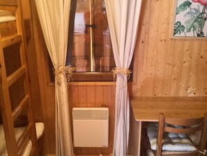 Quarto de cabana de madeira com janela, radiador e cama com encosto.