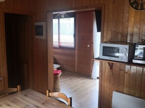 En inredning med träpanel, ett matbord, stolar, en mikrovågsugn och ett litet bord med en korg.