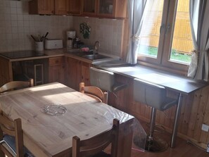 Ett kök med träskåp, en diskho, ett fönster med gardiner och ett matbord med stolar.
