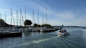 Ein Yachthafen mit mehreren Segelbooten an den Liegen, einem fahrenden Motorboot und einem wolkenlosen Himmel.