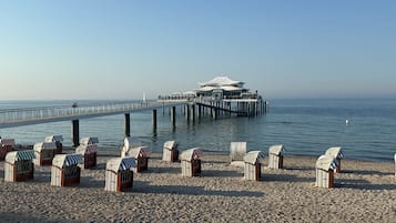 Una playa con cabañas de playa y un muelle que lleva a un edificio moderno con techo abovedado.