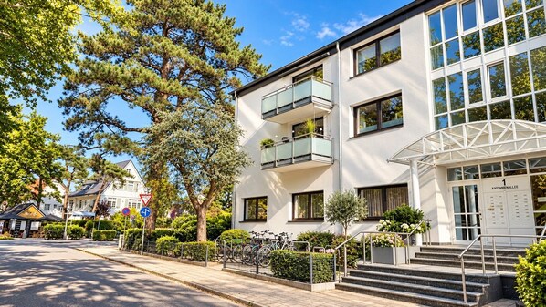 Ein mehrgeschossiges Gebäude mit einem Balkon im zweiten Stock, einer Treppe, die zum Eingang führt, und blauem Himmel.