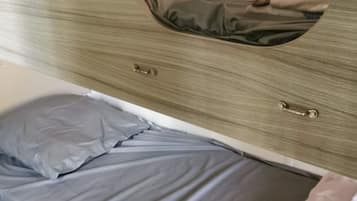 Un letto con materasso e cuscini grigi, un armadio in legno con uno specchio e un comodino.