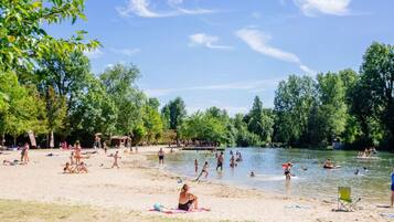 Una spiaggia sul lago, con persone che nuotano e si rilassano, circondata da alberi.