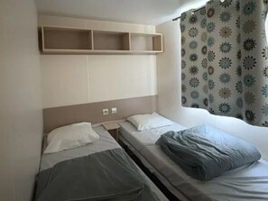 Ein Einzelbett mit Kopfteil, ein Nachttisch und ein Fenster mit gemusterten Vorhängen.