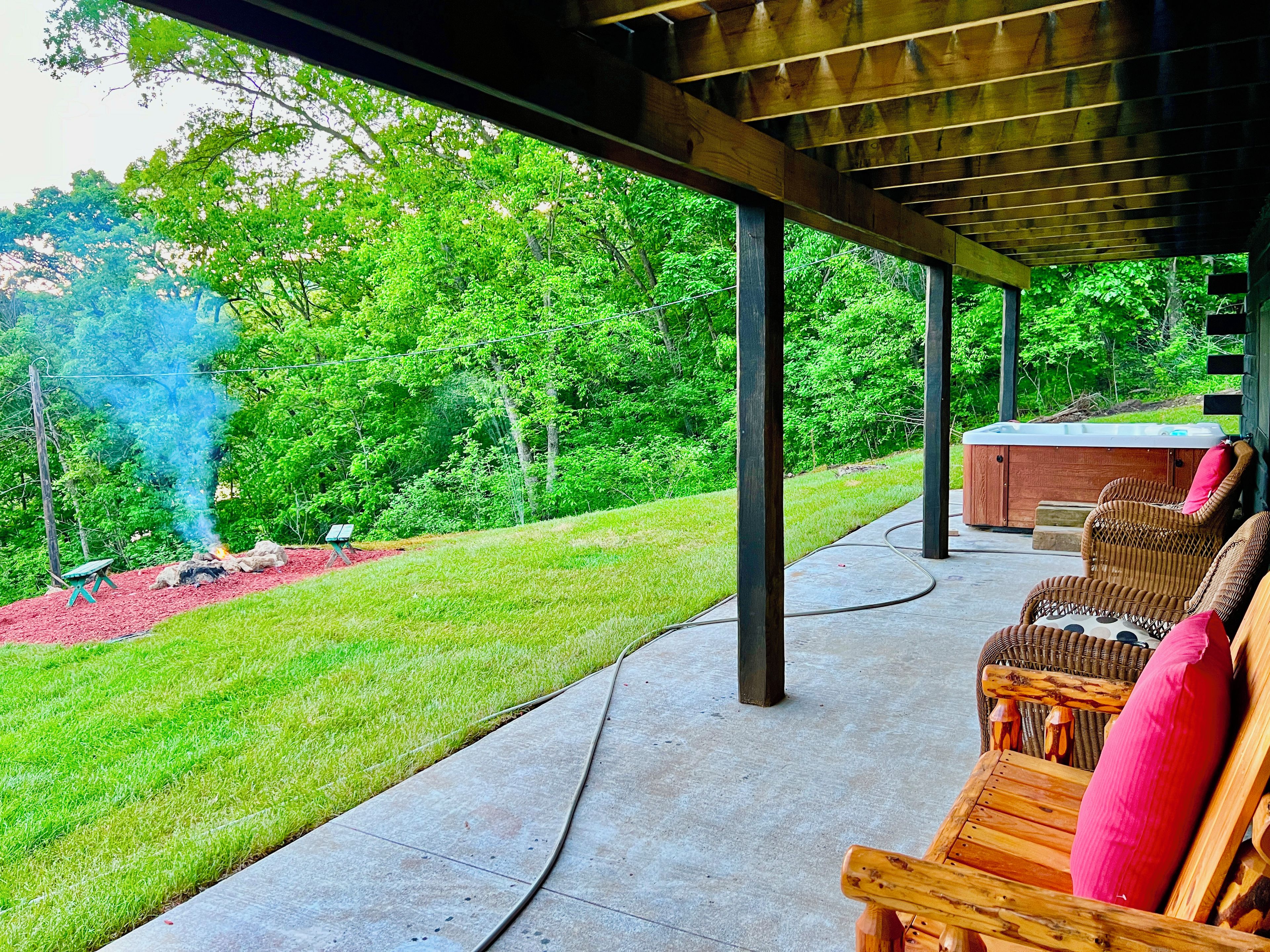 A covered outdoor area with a hot tub, wicker chairs, and a fire pit.