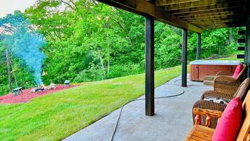 A covered outdoor area with a hot tub, wicker chairs, and a fire pit.