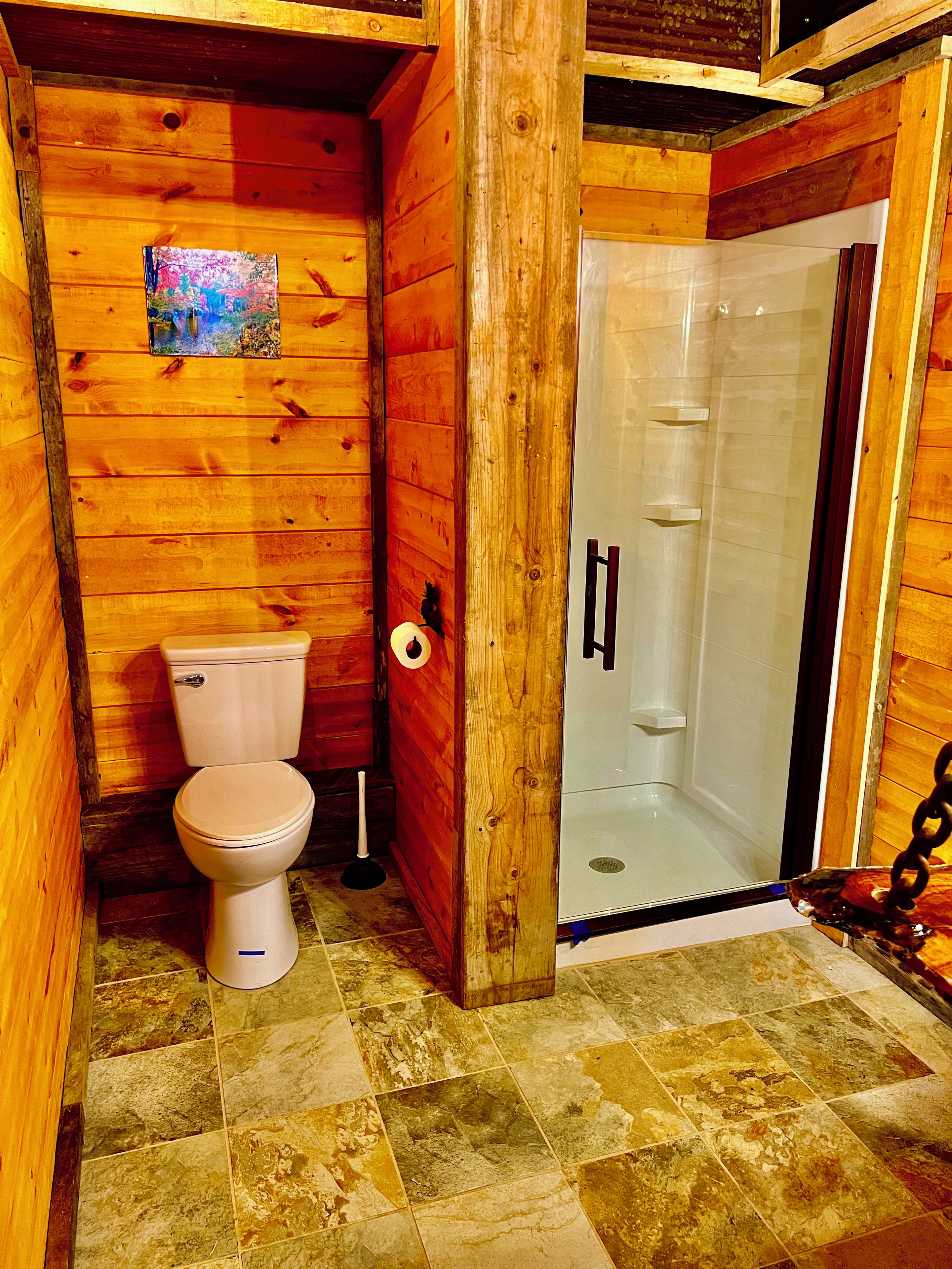 A wooden bathroom with a toilet, a shower, and a tiled floor.
