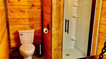 A wooden bathroom with a toilet, a shower, and a tiled floor.