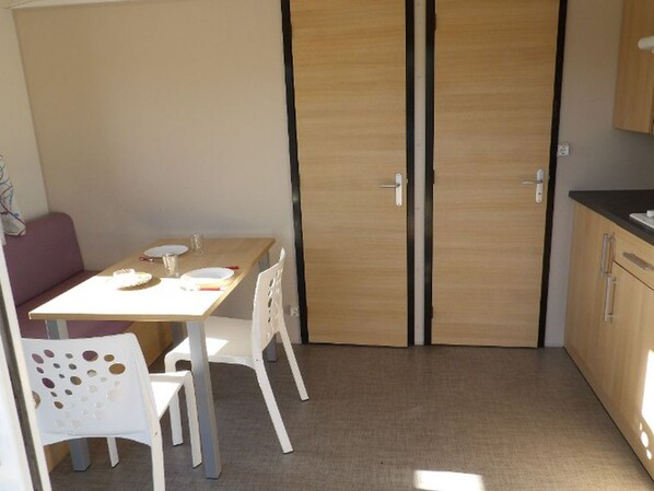 A compact room with a wooden door, a small table with chairs, and a kitchenette area.