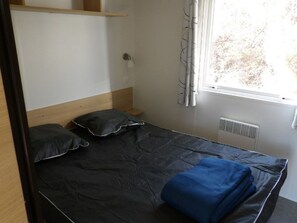 A single bed with a headboard, a bedside table, a lamp, and a window with curtains.
