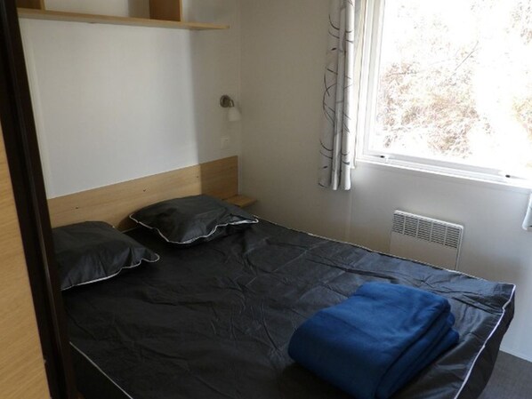 A single bed with a headboard, a bedside table, a lamp, and a window with curtains.
