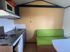 A compact kitchenette with a microwave, stove, and sink. - Cozy mobile home with terrace - 2 guests (Athée)