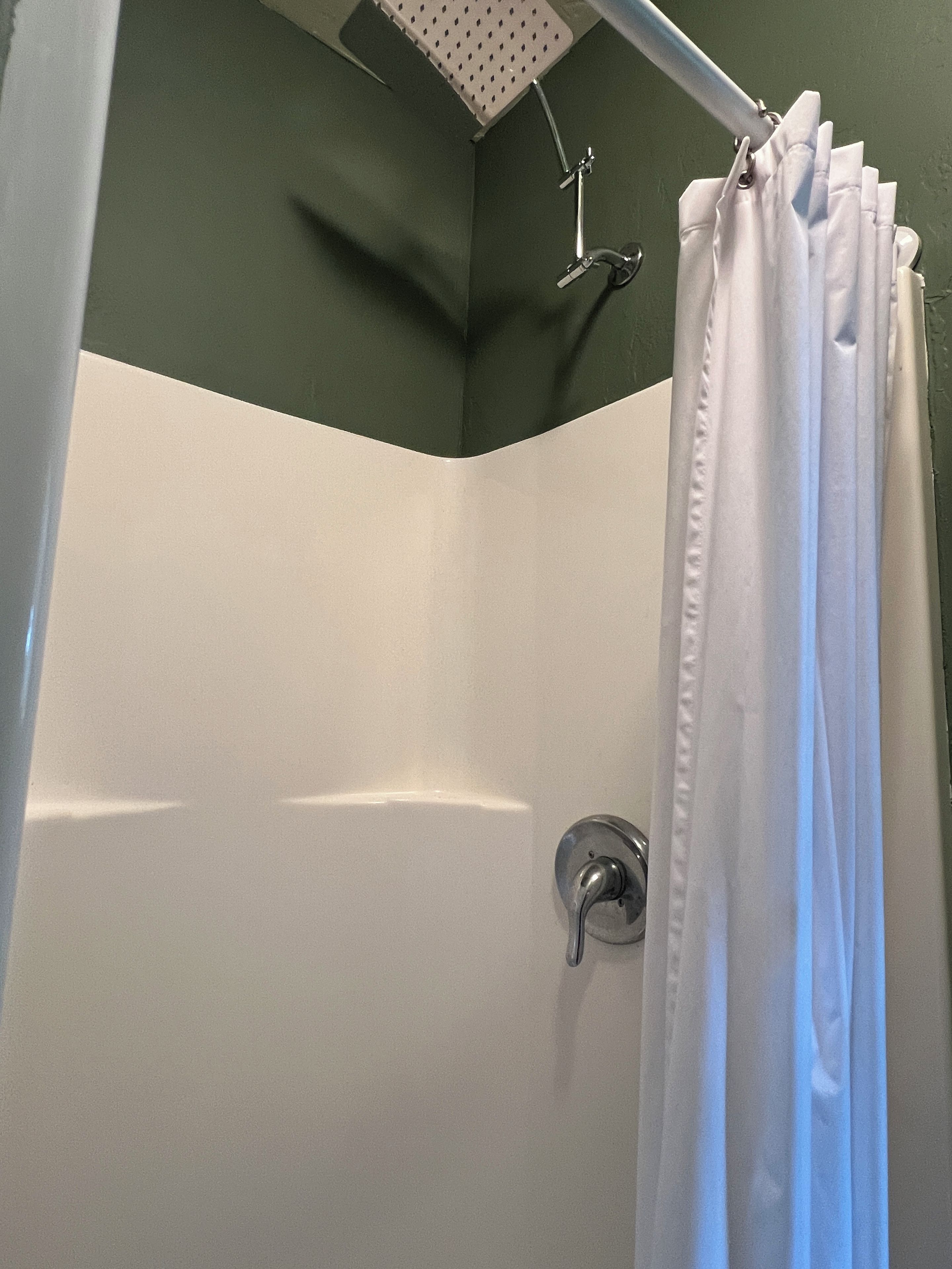 Zona de ducha con cortina blanca, rociador y pared con detalle en verde.