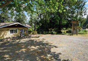 A gravel driveway leading to a yellow building with a porch, surrounded by trees and a wooden fence.